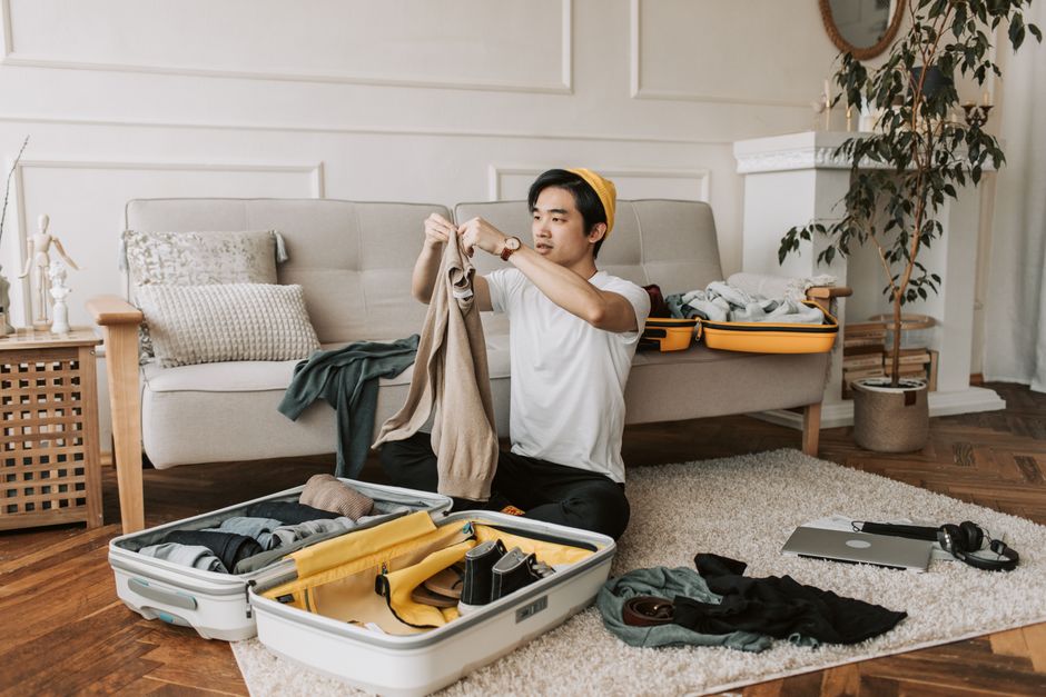 A person efficiently organizing a travel backpack with a laptop, various clothing items, and essentials, showcasing the importance of internal organization for a seven-day trip.