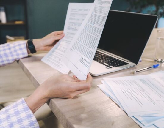 Close-up of a person's hands holding a magnifying glass over small text on a laptop screen, emphasizing the importance of reading online offer terms.
