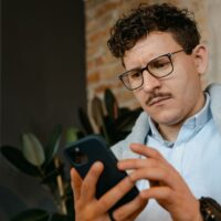 A person with a worried expression, squinting at very small text on a smartphone screen, representing the difficulty of reading online offer terms and conditions.