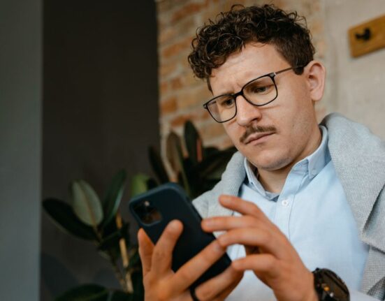 A person with a worried expression, squinting at very small text on a smartphone screen, representing the difficulty of reading online offer terms and conditions.