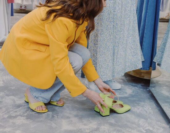A person sitting on a bench in a shoe store, trying on a pair of athletic shoes, with various shoeboxes in the background.