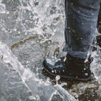 Person wearing stylish waterproof sneakers walking on a wet city street, light rain falling