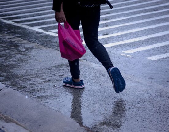 A person in comfortable waterproof shoes walks through a reflection on a wet city street, avoiding puddles.