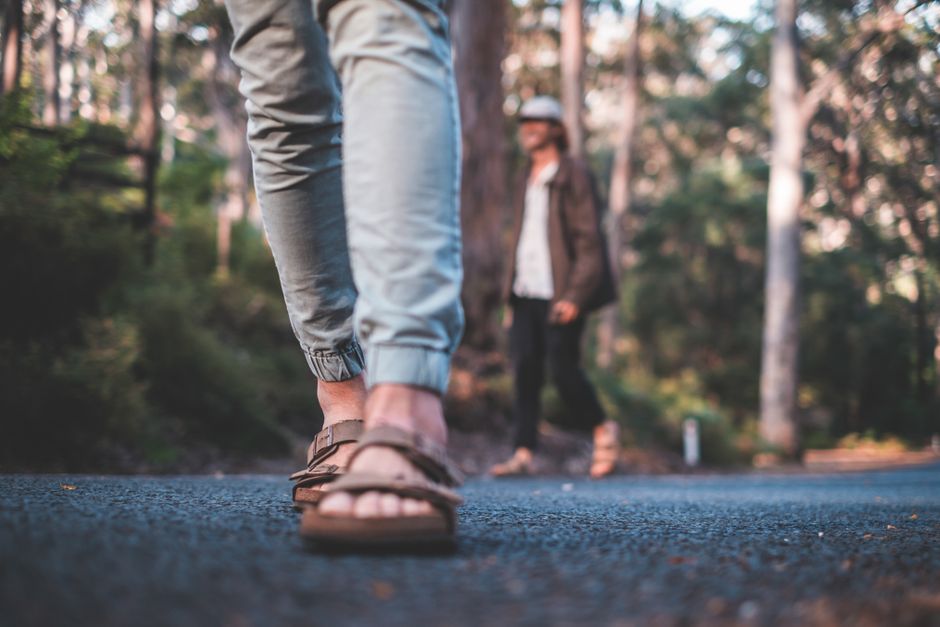 A person's feet, clad in highly adjustable and durable walking sandals, traversing a scenic, slightly uneven path, emphasizing secure fit and outdoor readiness.