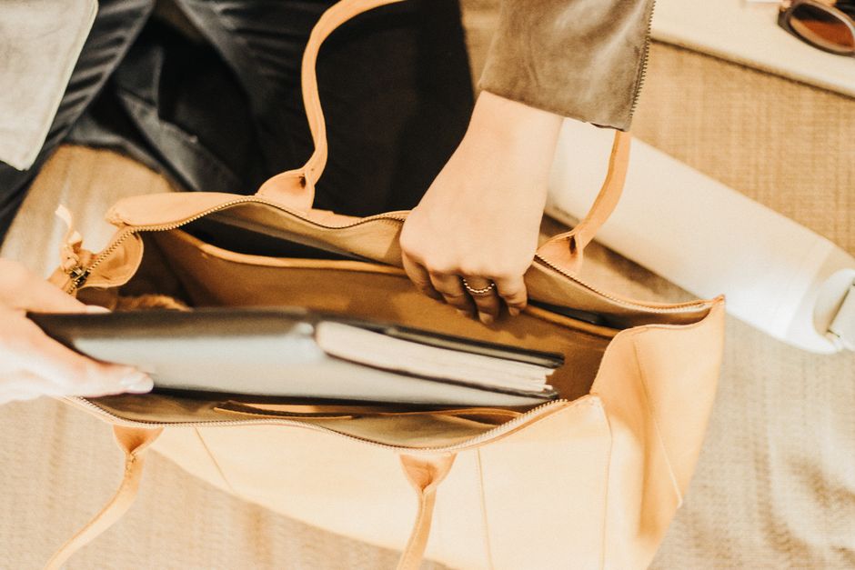 A professional holding a stylish and structured leather tote bag with a visible laptop compartment and small pockets for a phone and pens, suitable for work.