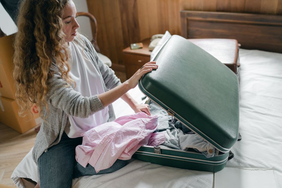 Young woman carefully folding clothes and packing a sleek, neutral suitcase for a trip.