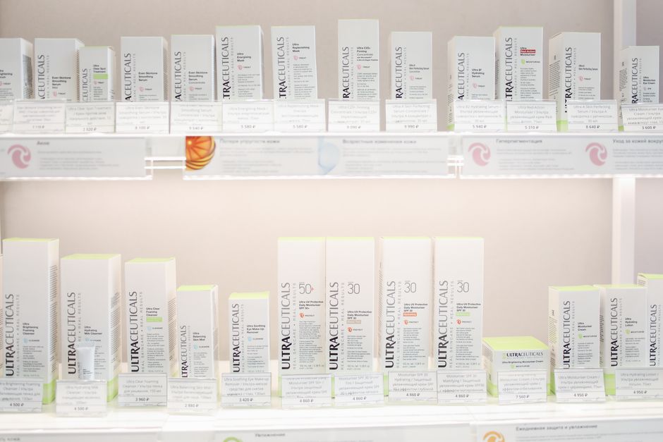 Close-up of various light-textured skincare products like serums, gel cleansers, and SPF bottles arranged neatly on a shelf.
