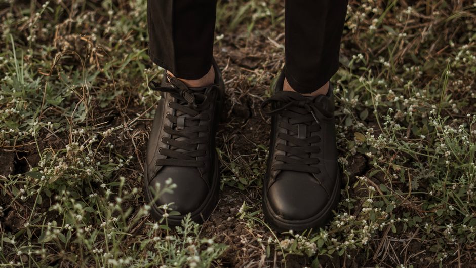 Close-up of a man's feet wearing clean white leather minimalist sneakers with dark tailored trousers, suitable for a sophisticated smart casual look.