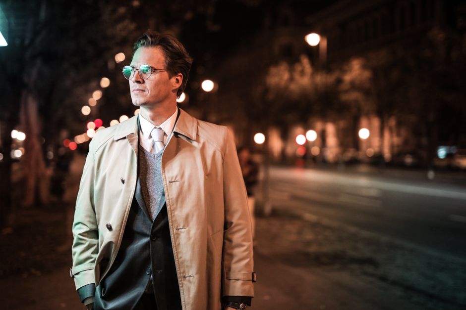 A stylish man in a classic trench coat walking through a European city, showcasing versatile outerwear from a capsule wardrobe.