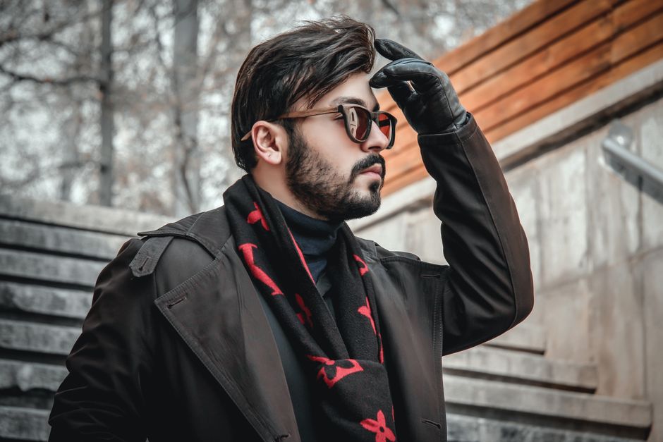 Close-up of a man wearing a cashmere scarf and leather gloves, looking warm and stylish in a cold city.