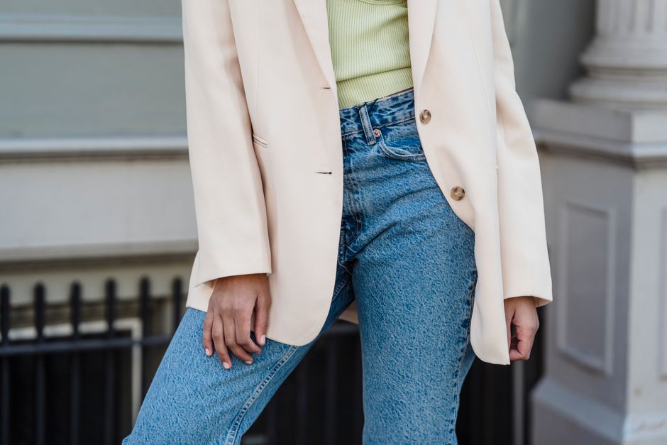 A stylish woman in a tailored blazer and trousers adjusting her sleeve, showcasing the importance of fit in creating elegant, affordable outfits.