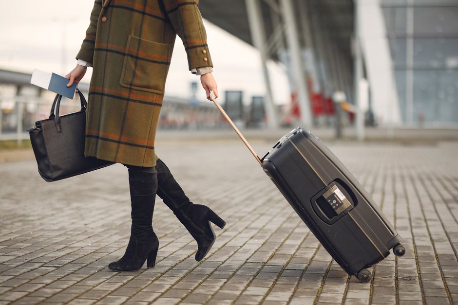 A woman in a chic yet comfortable travel outfit, consisting of a blazer, wide-leg trousers, and sneakers, confidently walks through a modern airport terminal.