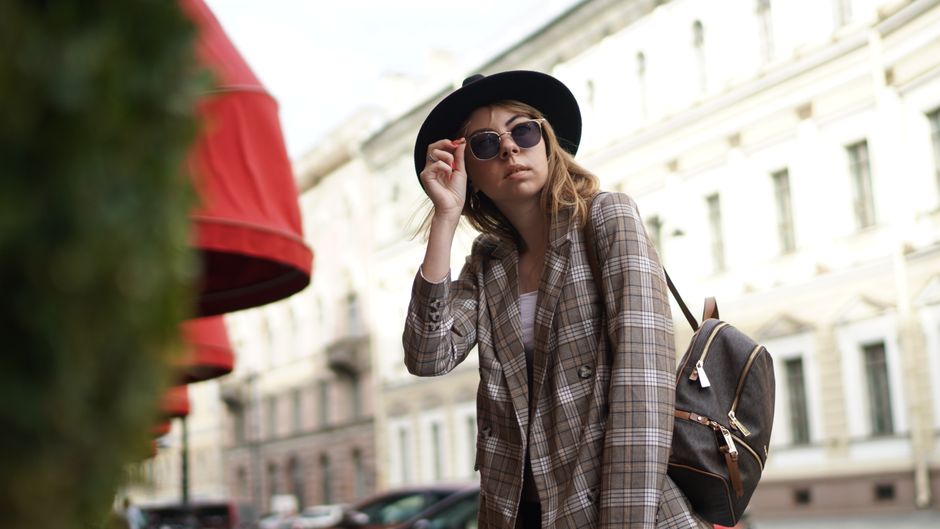 Fashionable woman in a trench coat and neutral trousers walking confidently down a European city street, showcasing a versatile capsule outfit.