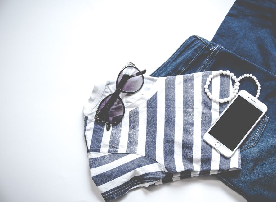A flat lay of a women's summer capsule wardrobe for humid weather, featuring linen trousers, a cotton top, sandals, a straw hat, and a versatile midi dress.