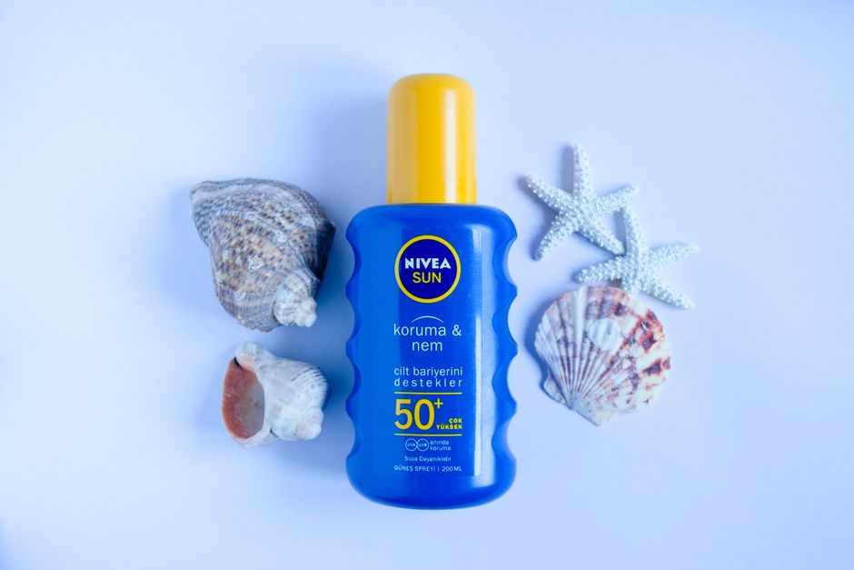 A person reapplying sunscreen with a spray mist over their makeup on a busy city street, sunglasses on head, looking refreshed.