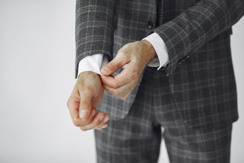A close-up shot of a tailor's hands adjusting the sleeve of a men's suit jacket, emphasizing the importance of fit.