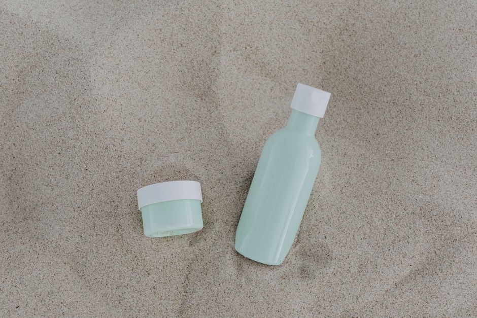 A neatly organized flat lay of various travel-sized beauty products: hydrating serum, rich face cream, lip balm, and hand cream, all under 100ml.