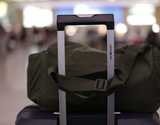 A person at an airport placing their black carry-on suitcase into an airline-provided sizer to confirm it meets dimension requirements.