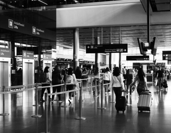A traveler at an airport gate measures their carry-on laptop backpack against a size checker, ensuring it meets airline dimensions.