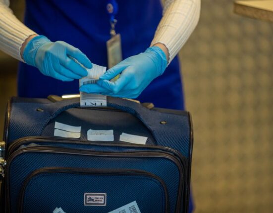 A person placing a soft-sided travel backpack into an airline sizer to check dimensions for a budget flight.