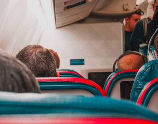 A person easily sliding a black personal item backpack under an airplane seat on a budget airline.