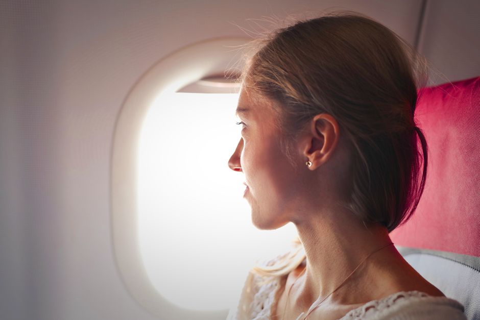 A traveler in casual, comfortable clothes with a cozy blanket, gazing thoughtfully out of an airplane window during a long journey.
