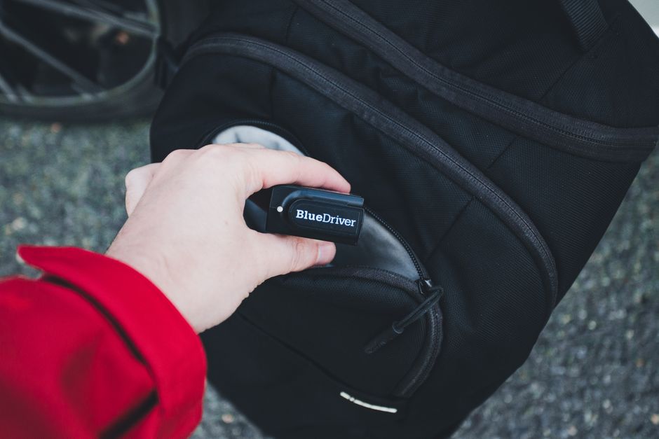 A traveler in an airport terminal demonstrating the lockable zippers on their anti-theft laptop backpack, holding a small padlock.