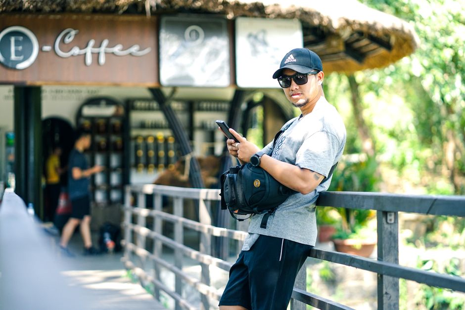 A person seated at an outdoor cafe table in Europe, using a compact anti-theft crossbody bag, secured to a chair leg.
