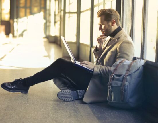 A traveler sits in an airport lounge with their laptop bag next to them, open, showing organized contents like a laptop and documents, emphasizing readiness for remote work and travel.