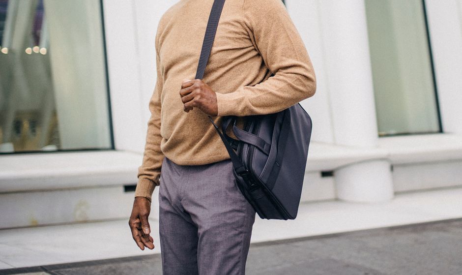 A traveler in a train station securely wearing an anti-theft crossbody bag, checking phone.