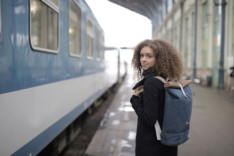A commuter wearing a small, ergonomic backpack while waiting at a busy city train station, highlighting its utility for daily travel.