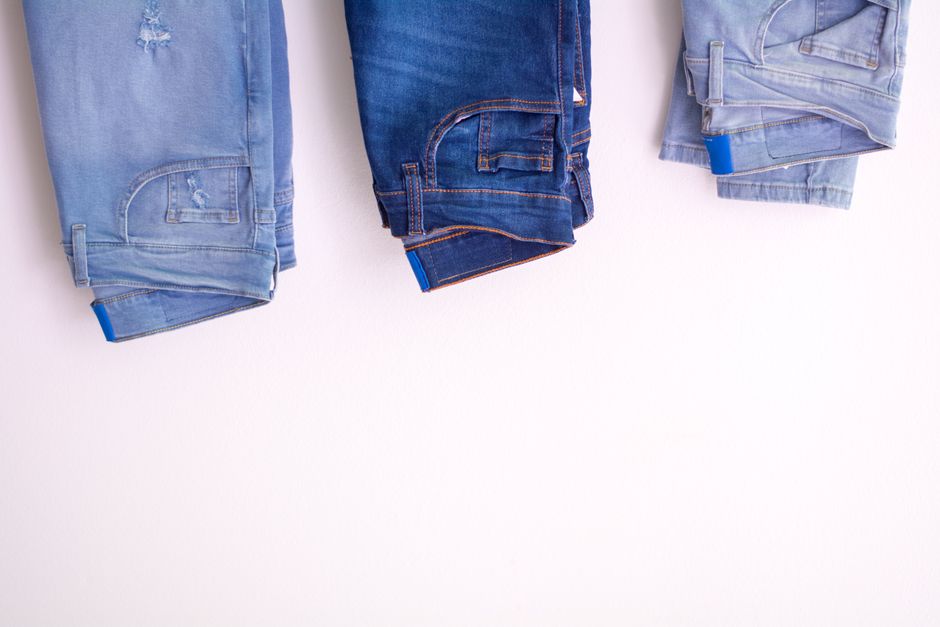 A close-up shot showing the different textures and colors of various denim washes, from dark indigo to light blue, highlighting the fabric details.