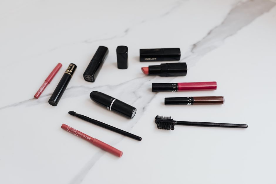 A flat lay of practical travel makeup items, including a solid cleansing balm, a multi-stick for lips and cheeks, a mini setting spray, and a small SPF bottle.