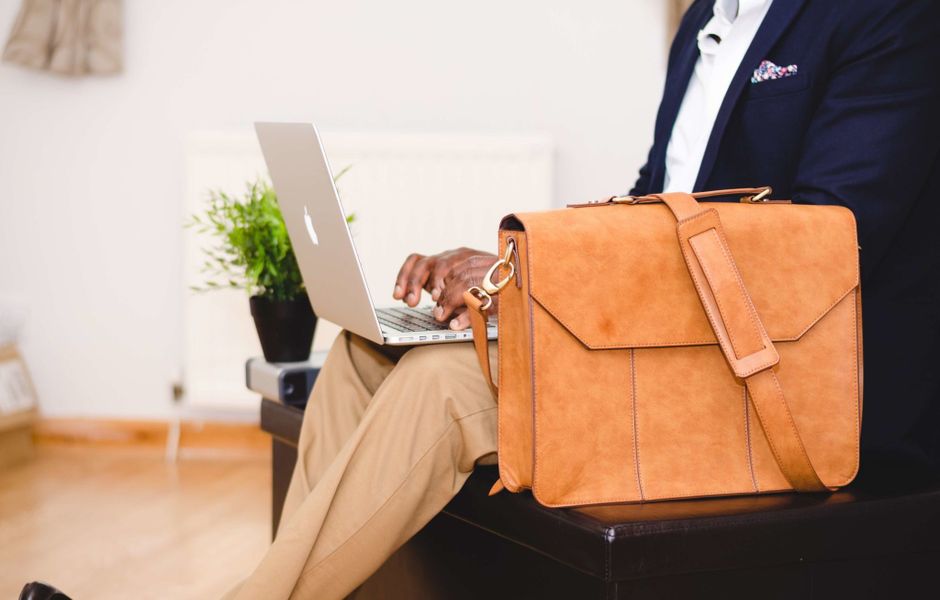 A sleek, minimalist vegan leather briefcase, in a neutral tone, sitting on a contemporary office desk next to a laptop and a coffee cup, illustrating a practical choice for work.