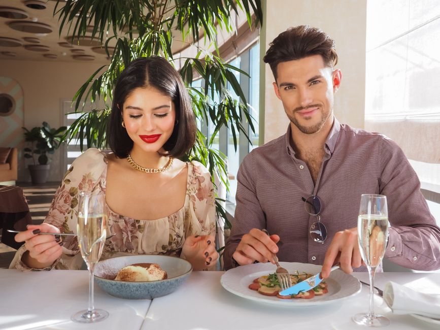 Well-dressed man in a blazer and button-down shirt at a restaurant table, looking confident.