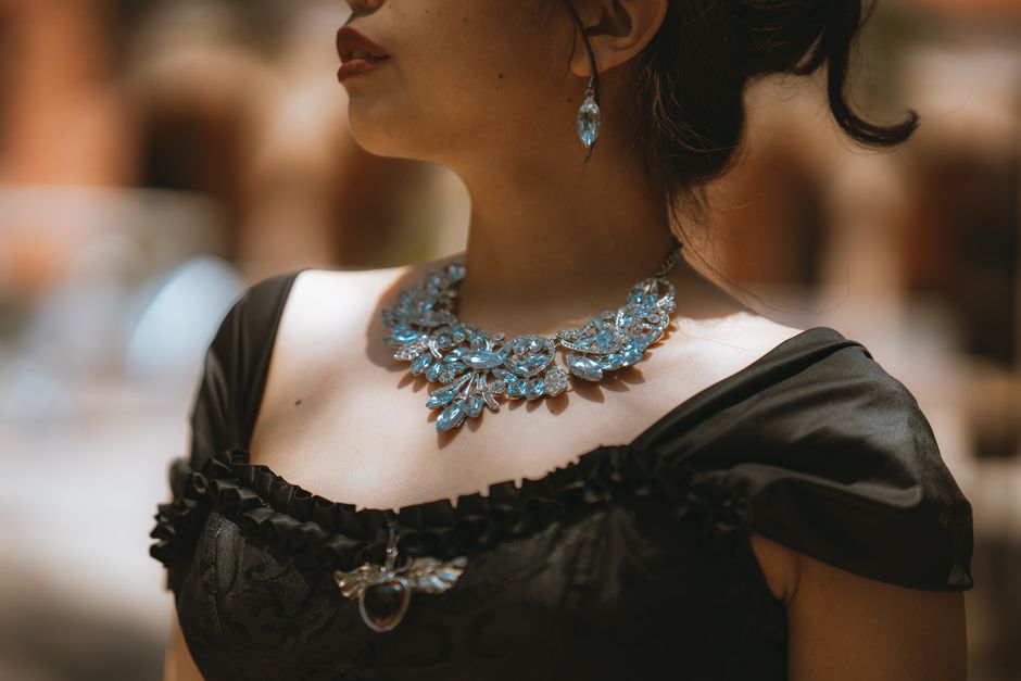 A close-up of a woman's hands adding a delicate gold necklace to a simple black top, highlighting the transformative power of accessories.