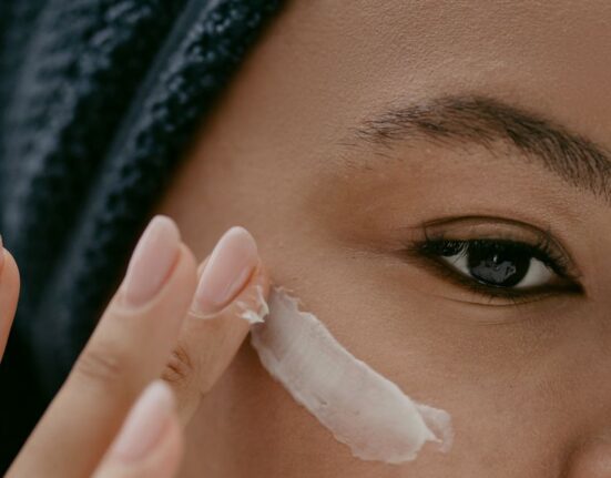Woman gently applying moisturizer to her face on an airplane seat, looking refreshed.