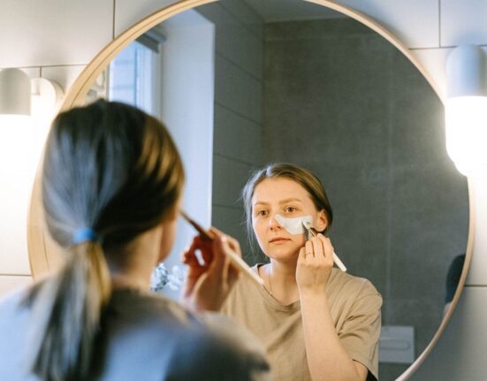 A woman quickly dabbing tinted moisturizer onto her face in a well-lit bathroom, symbolizing a fast and effective morning routine.