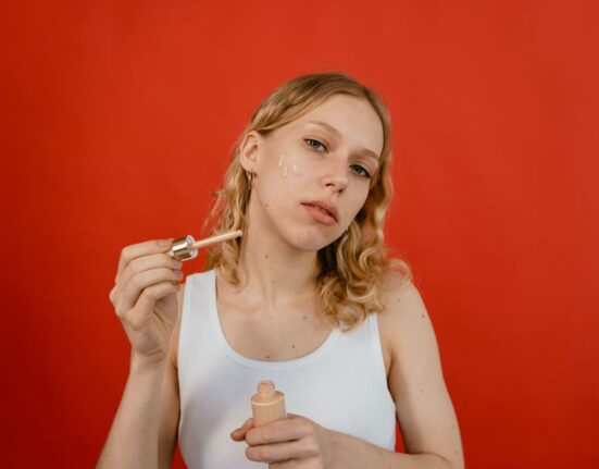 A woman gently applying a lightweight serum to her face in a bright, humid environment.
