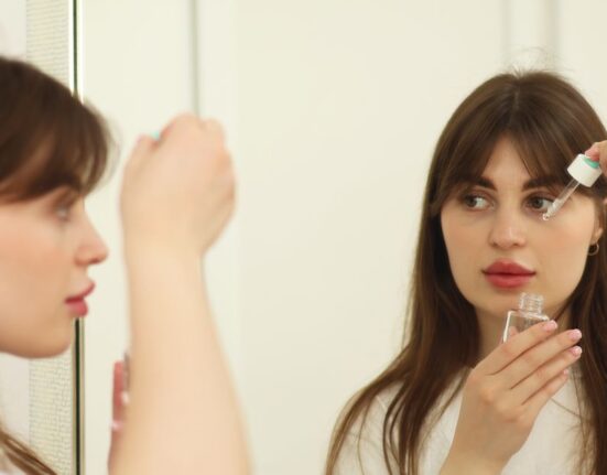 A woman in her 30s gently applying a small amount of retinol serum to her face at night, with other skincare products blurred in the background, representing a mindful beginner retinol routine for adults.