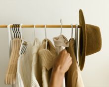 A woman thoughtfully organizing her capsule wardrobe with neutral clothing on hangers and folded items.
