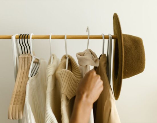 A woman thoughtfully organizing her capsule wardrobe with neutral clothing on hangers and folded items.