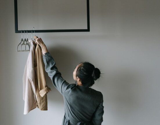A woman smiling as she organizes a minimalist closet filled with a neat, curated selection of neutral-toned clothing, showcasing a women's capsule wardrobe.