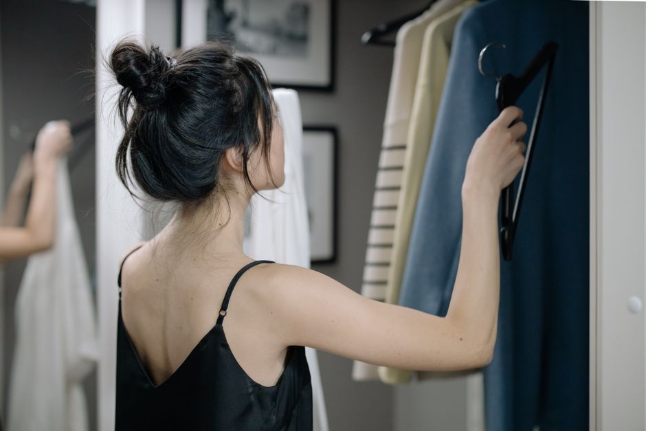 A woman thoughtfully selecting a top from her curated minimalist wardrobe, showcasing ease and intentionality in her daily routine.