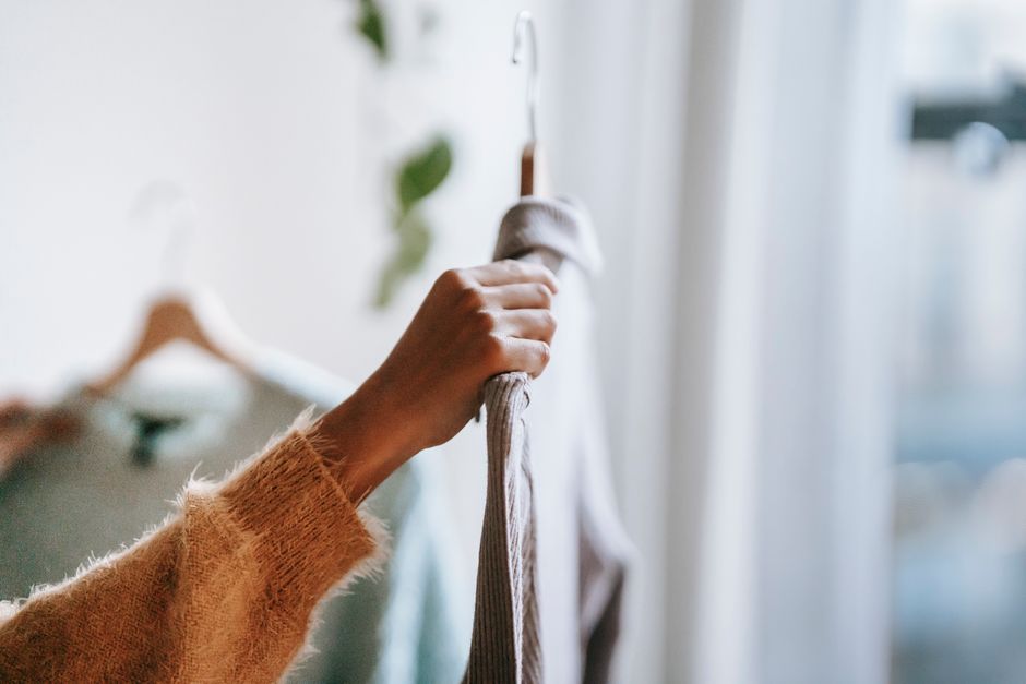 A woman standing in front of an open wardrobe, selecting a white shirt from a curated collection of minimalist clothing in neutral tones, exemplifying versatility.