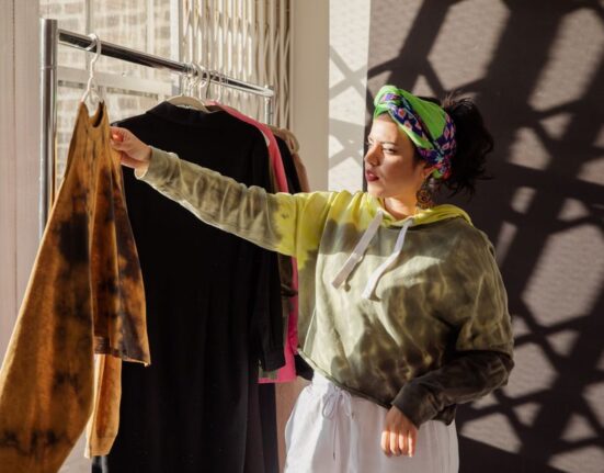 A woman thoughtfully examining a rack of clothing made from natural fibers in a well-lit boutique, symbolizing conscious shopping.