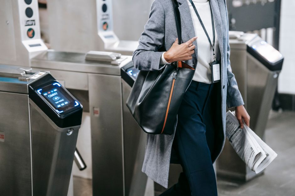A professional woman walking confidently on a city street, carrying a structured tote bag and wearing a classic trench coat over tailored workwear, suitable for commuting to a hybrid office.