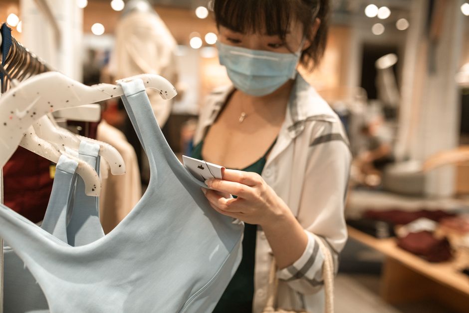 A woman in a clothing store thoughtfully examining a price tag, representing the critical evaluation needed to discern genuine discounts during seasonal sales.