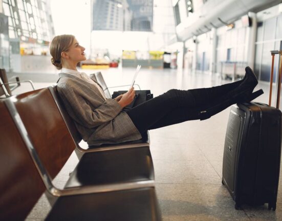 Woman comfortably seated in an airport lounge, wearing loose-fitting, stylish travel clothes, looking at her phone.