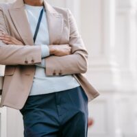 A confident woman in a classic navy blazer and tailored beige trousers walking purposefully on a city street, carrying a structured handbag, embodying easy workwear outfits for hybrid offices.